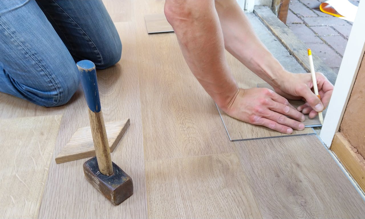 services-01 A craftsman carefully measures and marks wooden floor panels for precise installation.